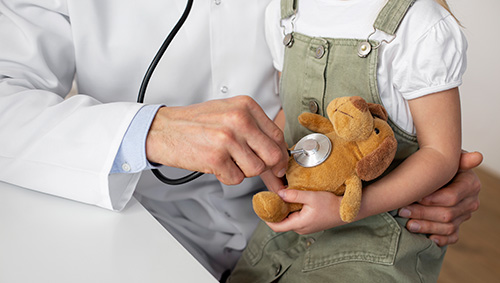 kind pediatrician using a stethoscope on a child's teddy bear